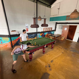 Two backpackers lining up shots at the snooker table, surrounded by fellow guests enjoying the vibe.
