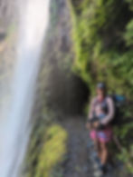 Smiling thru-hiker standing beside Tunnel Falls on the Eagle Creek Trail, a popular alternate near the end of the Oregon PCT section