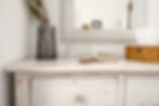 A white dresser with a reusable water bottle, a vase of fresh flowers, and soft reflections in the mirror offering a glimpse into a serene bedroom setting.