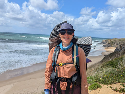 Hiker smiling with windswept hair and dramatic coastal cliffs in the background on Day 2 of the Fisherman’s Trail in Portugal.