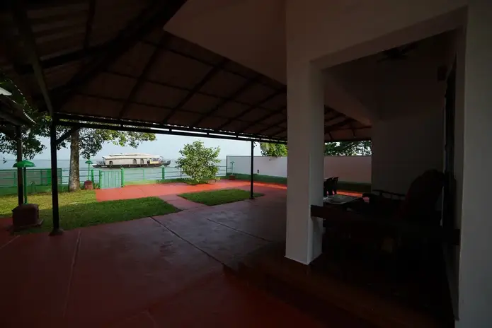 View from the porch of Lake facing Cottage, of Lake front. Houseboat passing through in the Lake in background. At Illikkalam Lakeside Cottages, Kumarakom