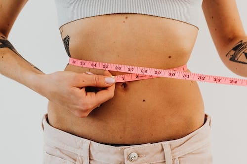 A women measuring her waist size for BMI with an inch tape.