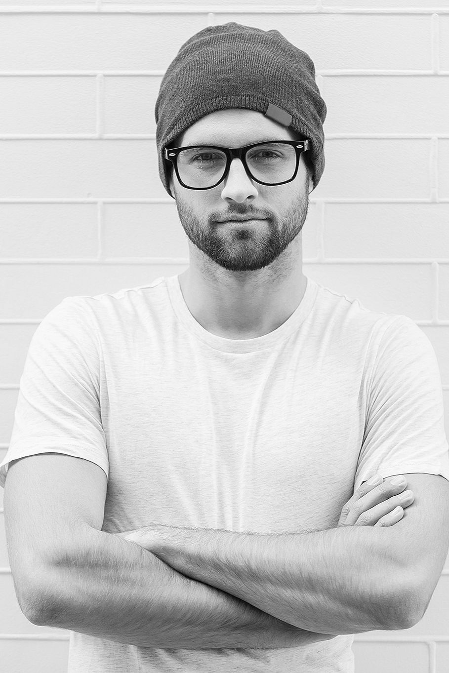 Team Headshot — 922 Designs creative professional in beanie and glasses against a white brick wall (black-and-white portrait)