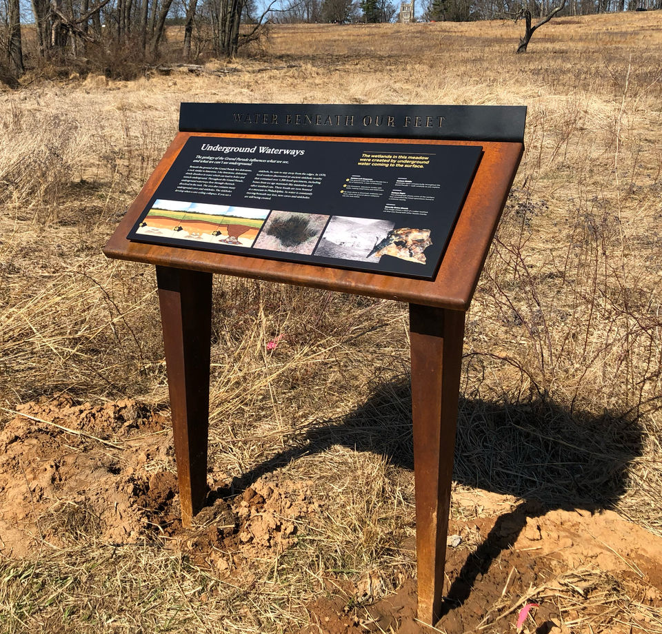 Informational sign titled “Underground Passages” about the area's natural history, set on a metal frame over a patch of dirt and dry grass.