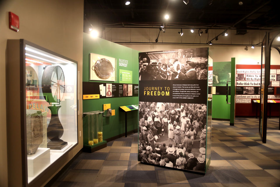 Civil rights-themed exhibit with interpretive panels and a large photo display titled “JOURNEY TO FREEDOM,” flanked by artifact cases and green walls.