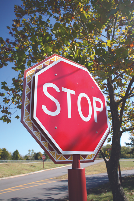 Decorative stop sign with a patterned base located at a vehicular junction inside the zoo campus.