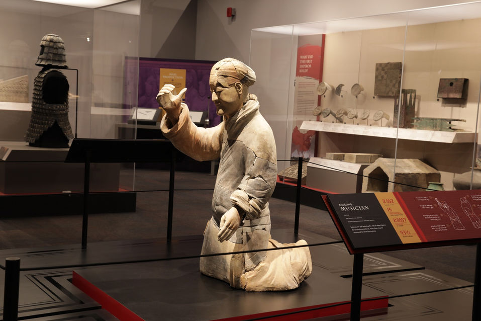 Life-size terracotta kneeling archer statue in a display case with interpretive text explaining armor and battle posture.
