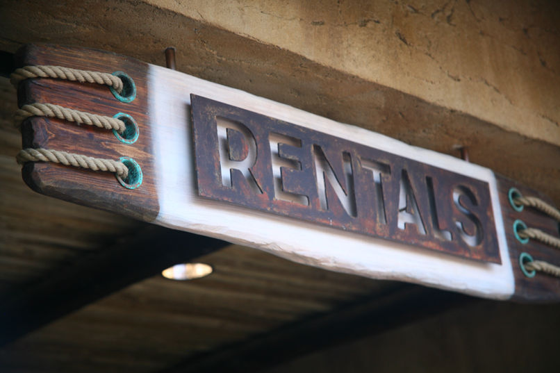 Rustic wooden “RENTALS” sign with decorative rope ends, mounted under a canopy.