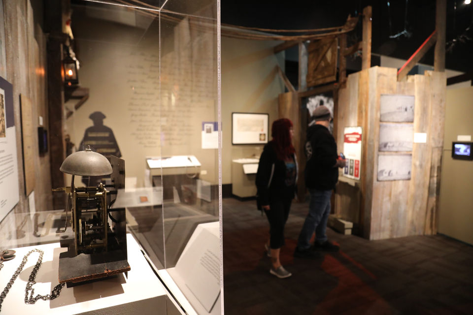 A glass display case showcases a historic artifact under soft lighting, surrounded by layered exhibit elements, graphics, and walk-through areas.