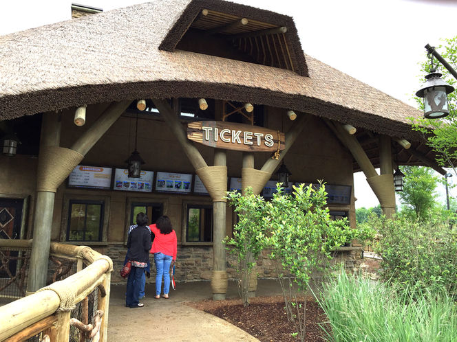 Thatched-roof ticket booth entrance with “TICKETS” sign and guests entering.
