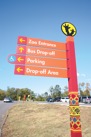 Color-coded directional sign pointing to zoo entrance, bus drop-off, parking, and drop-off area, with accessibility symbol.