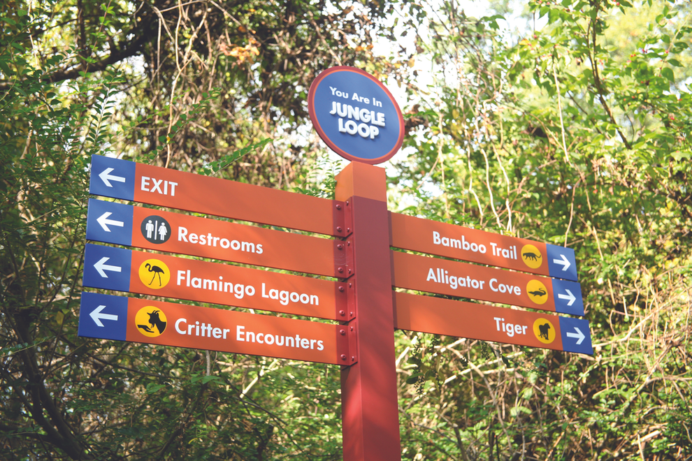 Orange and blue directional signage pointing to exits, restrooms, and exhibits like Alligator Cove and Critter Encounters.