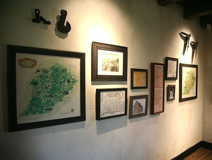 Historic map and artifact gallery wall – A dark room with framed antique maps and early illustrations is accented with hanging blacksmith tools.