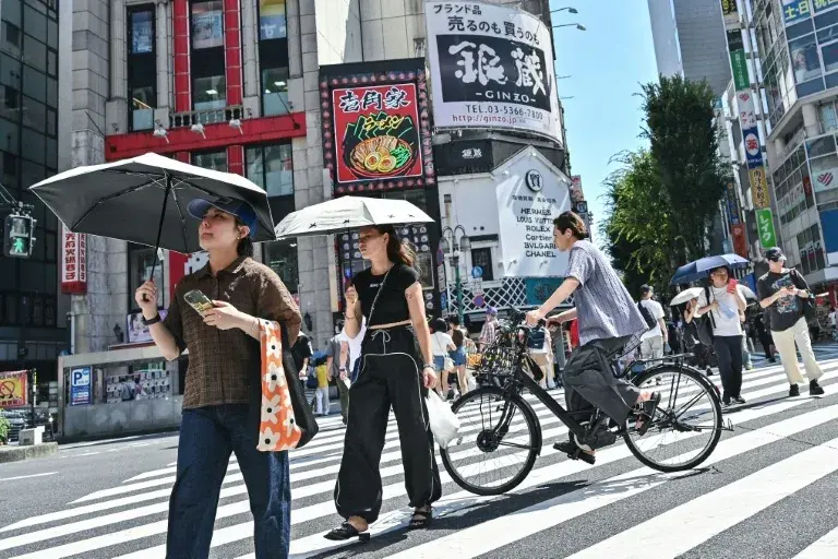 Pedestrians use umbrellas to shelter from the sun as they cross a street in the Kabukicho entertainment area of Shinjuku in central Tokyo (Richard A. Brooks) Richard A. Brooks/AFP/AFPLess