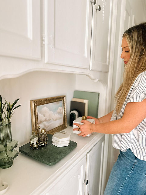 Woman arranging decor items including frames, on a white counter.