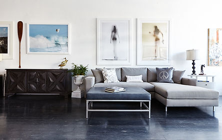 Image of showroom featuring gray sofa chaise, art on the walls, side consoles