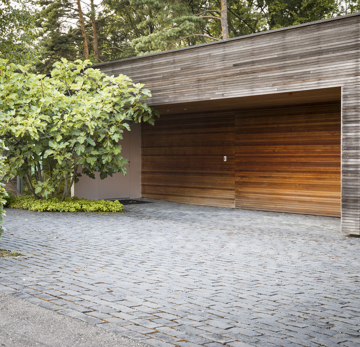 Moderne Holzgarage mit gepflasterter Einfahrt und üppigem Grün daneben.