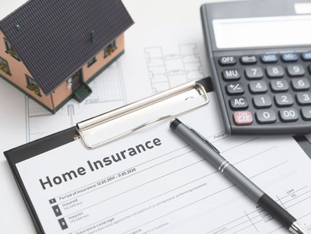 UK home insurance documents on a wooden desk with a house key and miniature model home.