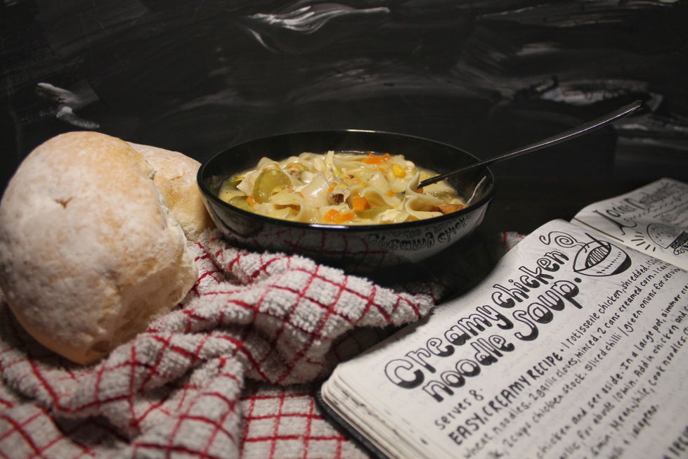Home styled food photography of chicken soup surrounded by rolls, cloth and a handwritten recipe