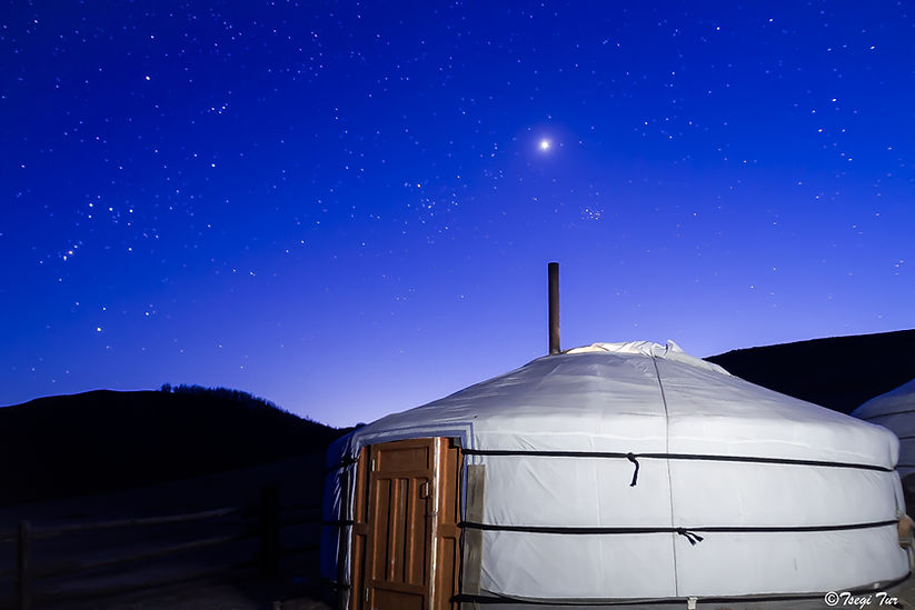 A single white Mongolian ger stands under a vibrant blue night sky filled with stars and a bright moon