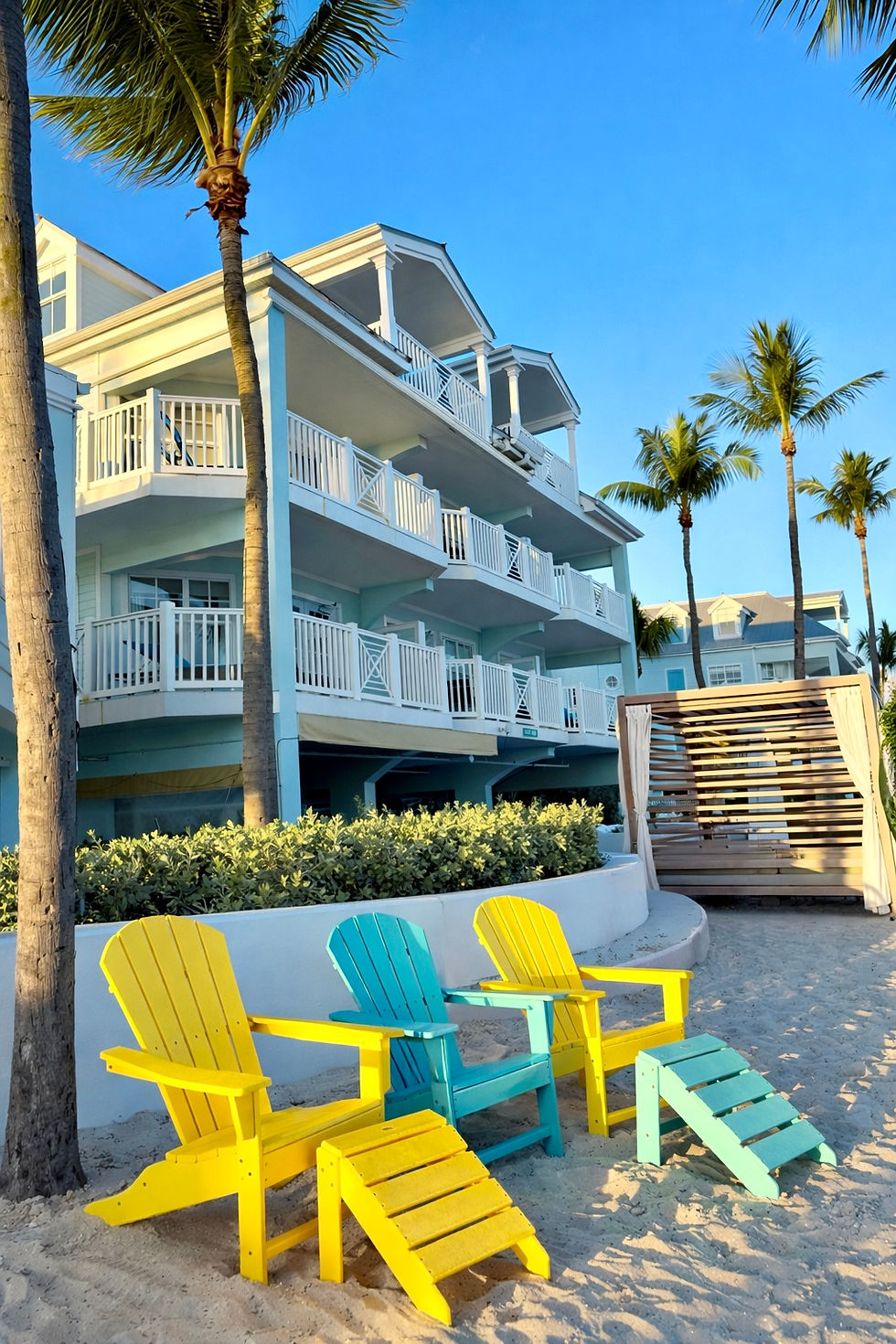 Beach resort with colorful Adirondack chairs under palm trees.