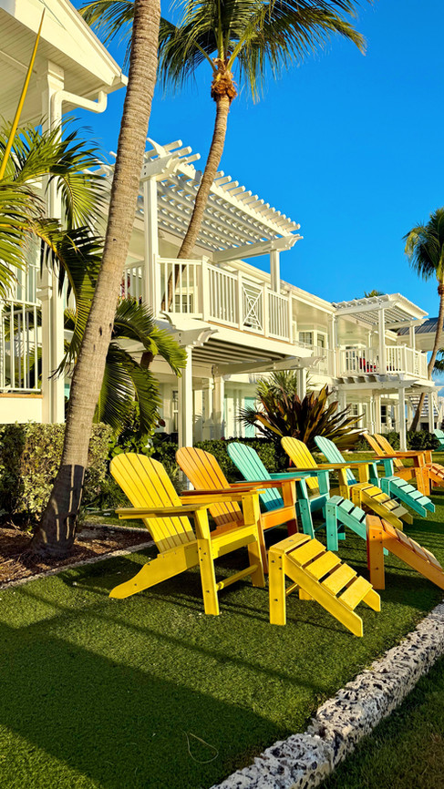 Colorful Adirondack chairs on the oceanfront lawn at Southernmost Beach Resort & Guesthouses with palm trees, tropical landscaping, and luxury guesthouse balconies in Key West, Florida.
