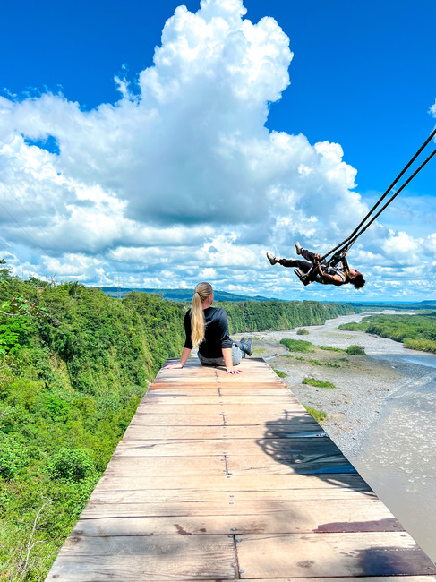 Woman sitting on a wooden platform overlooking a river valley while zipliners swing through the sky in Ecuador