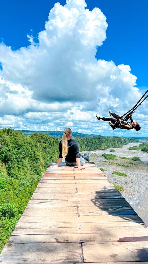 Woman sitting on a wooden platform overlooking a river valley while zipliners swing through the sky in Ecuador