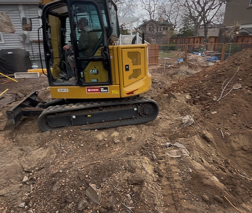 An excavator digging out the foundation for a new ADU installation in a homeowners backyard.