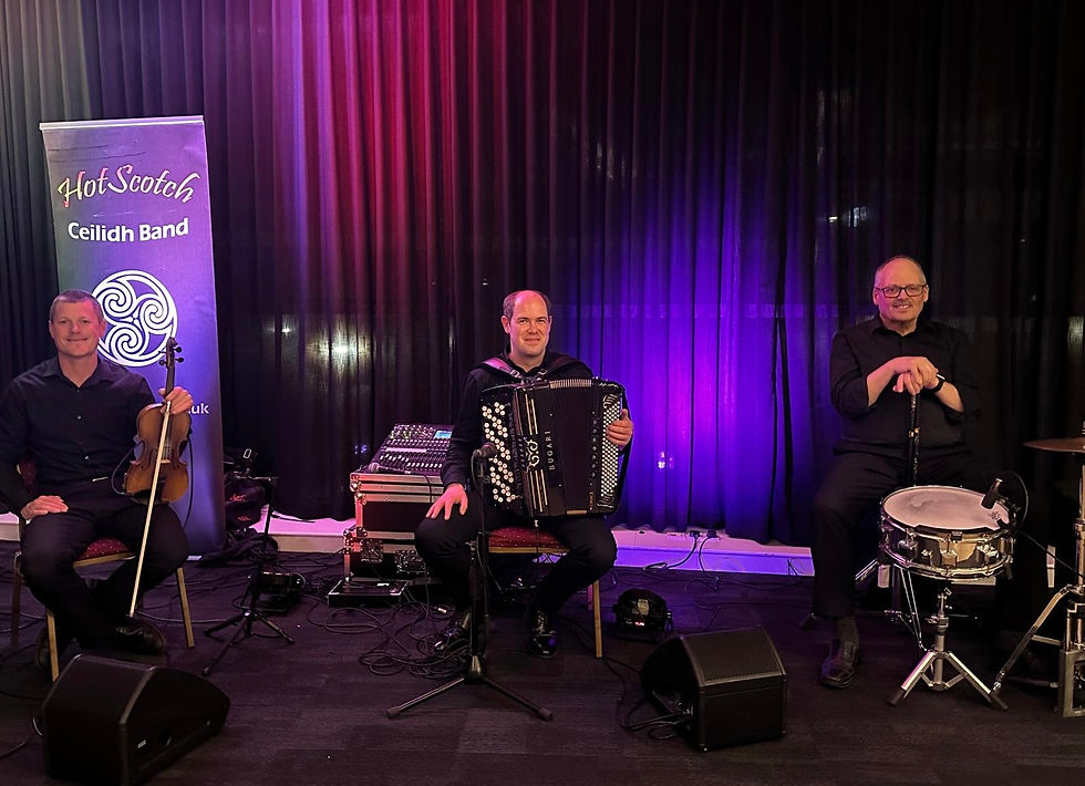 trio of accordion, fiddle and drums with HotScotch Ceilidh Band sign behind