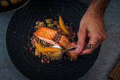 Hands plating a salmon dish on a black plate – food photography