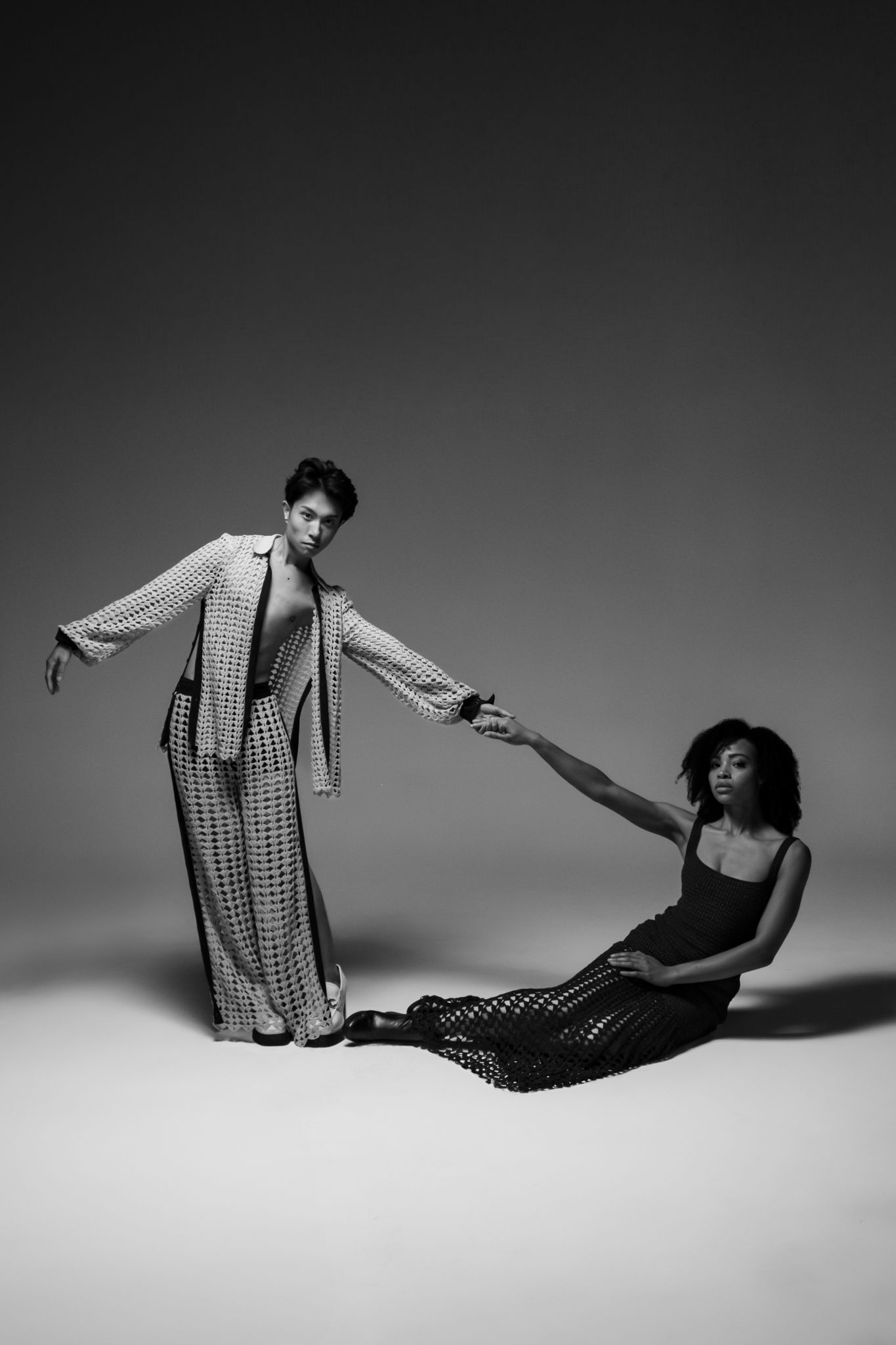 Two models posing in hand-crocheted cotton garments: a slate blue mesh pant set and a long dark blue crochet dress.