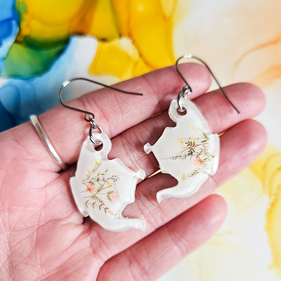 handmade white and wilflowers teapot resin earrings held in hands on abstract ink background