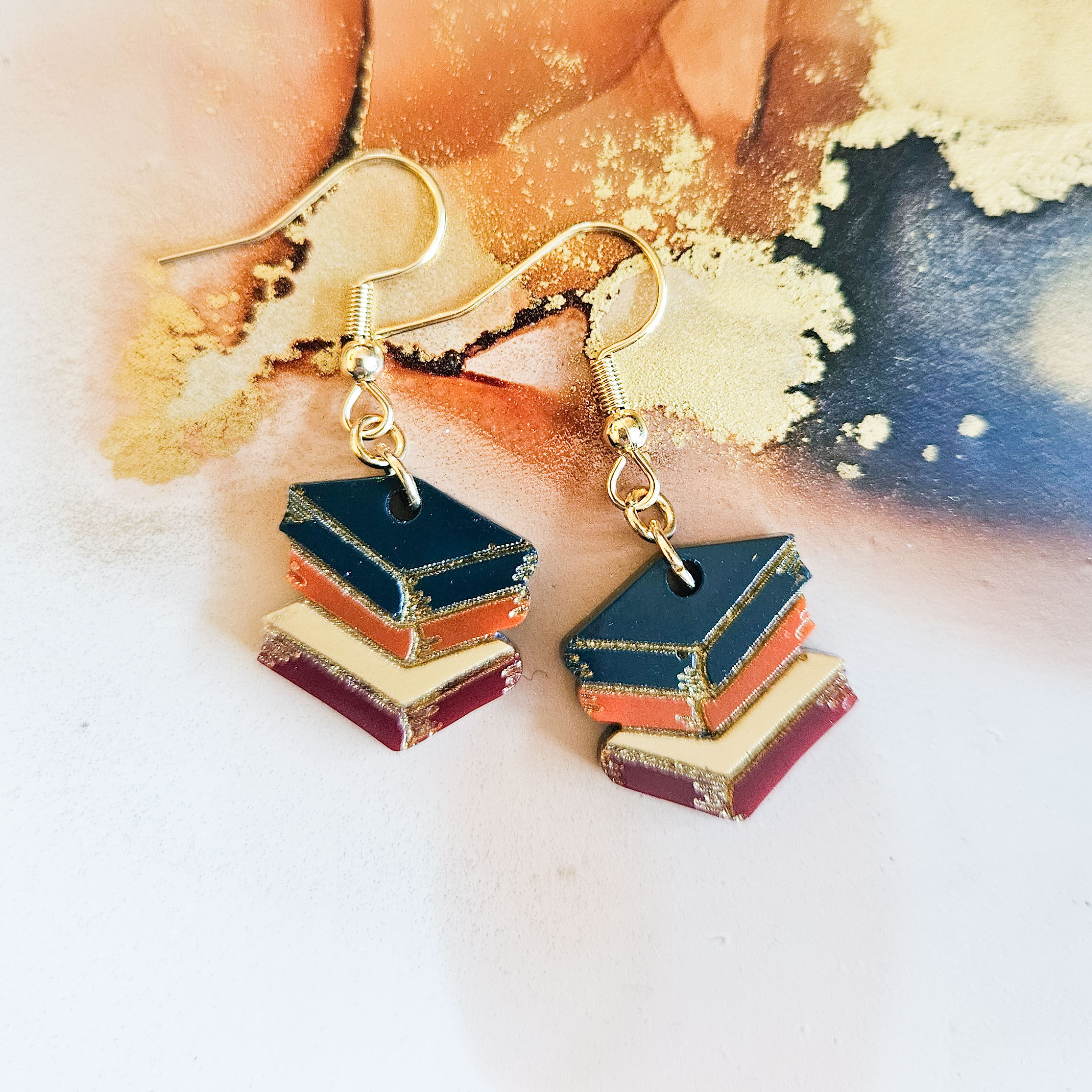 handmade book stack resin dangle earrings with gold plated stainless steel hooks on abstract background