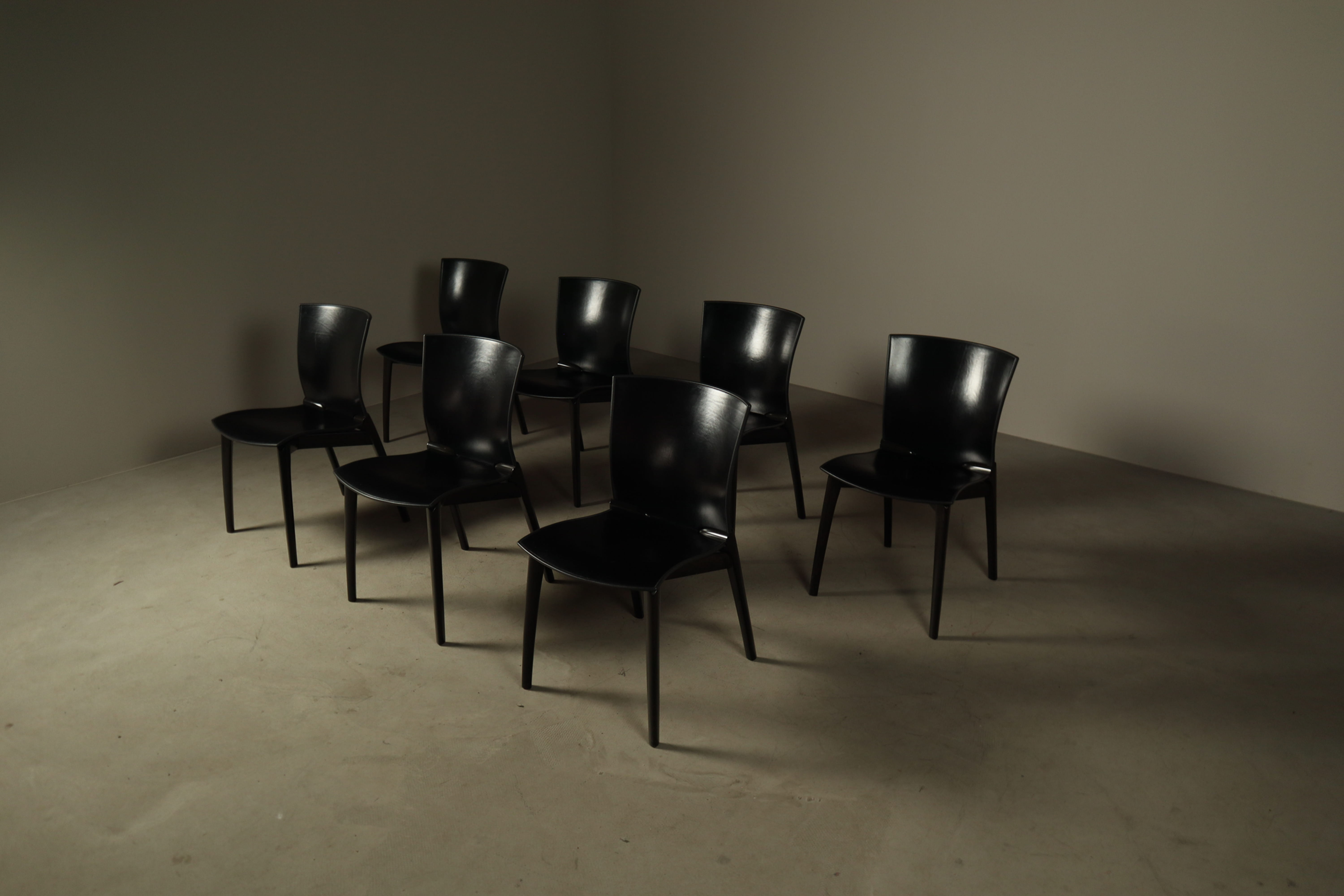 High-angle front studio composition of seven black Cassina COS chairs arranged in a loose semicircle.