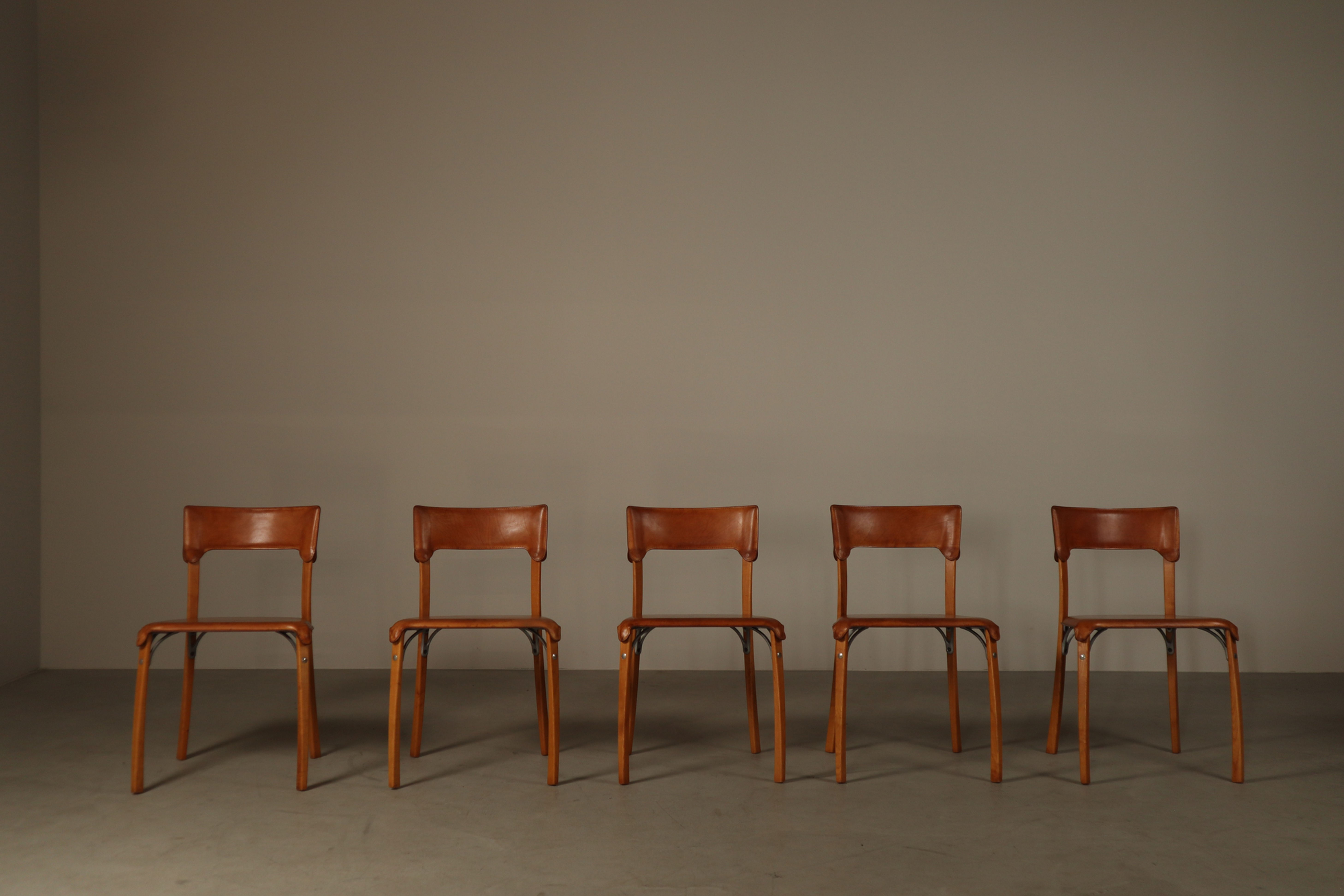 Five 1990s Italian dining chairs arranged side by side, with cognac leather upholstery and wooden frames.
