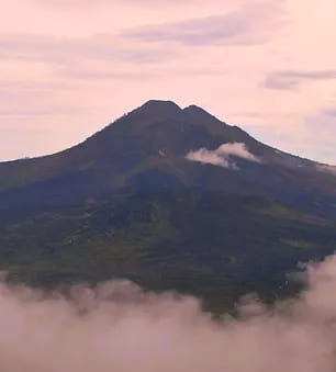 Il vulcano indonesiano Batur si erge regale sopra un mare di nuvole, con la cima sfumata in rosa dal sole al tramonto, simboleggiando la maestosa bellezza naturale e il potere imponente della terra