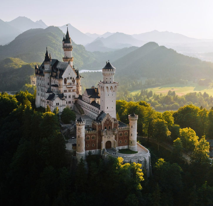 Neuschwanstein Castle perched above forested Bavarian hills, bathed in soft light on the German Alpine Road.