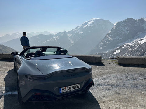 Grey Aston Martin Vantage Cabriolet parked on the summit of the Stelvio Pass with the driver admiring the surrounding peaks.