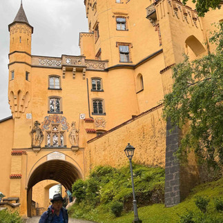 Visitor standing beneath the archway of a mustard-yellow hilltop castle with turrets and stone carvings.
