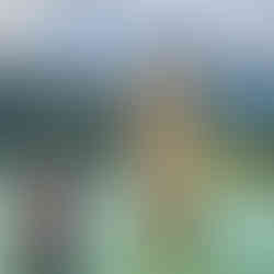 Woman in sunhat and striped top posing in front of the submerged church tower of Reschensee with forested mountains behind.