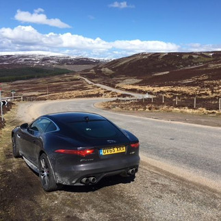 Black Jaguar F-Type stopped on an open moorland road with wide Highland views along the Snow Roads Scenic Route