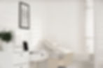 Modern, minimalist medical office with examination bed and desk.