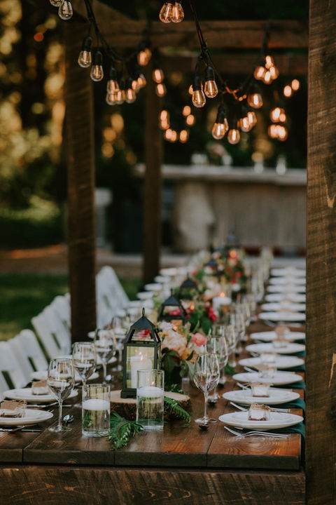 Long dinner table set with plates, glasses, and flowers at outdoor event.