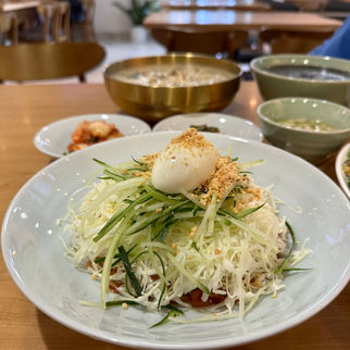 Chilled Jjolmyeon with chewy noodles in a secret savory sauce, topped with crisp cabbage, fresh cucumber slices, and a halved boiled egg, perfect for cooling off on a hot day in Hawaii 쫄면