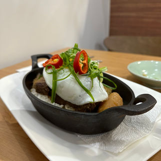 Marinated and braised kalbi beef served over rice in a cast iron dish, garnished with a sunny-side-up egg, sliced green onions, and chili peppers, accompanied by radish, carrot chunks, and mushrooms. 갈비찜
