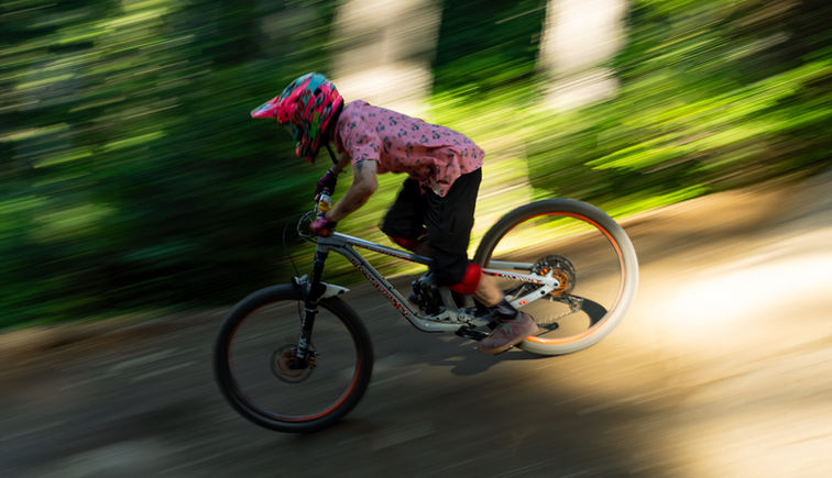 Downhill mountain biker riding fast through the forest in Whistler Bike Park with motion blur showing speed.