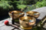 3 tibetan gold singing bowls with a red mallet and a black mallet resting on a wooden bench