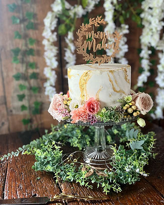 A small wedding cake with gold marbling and fresh flowers around the bottom.