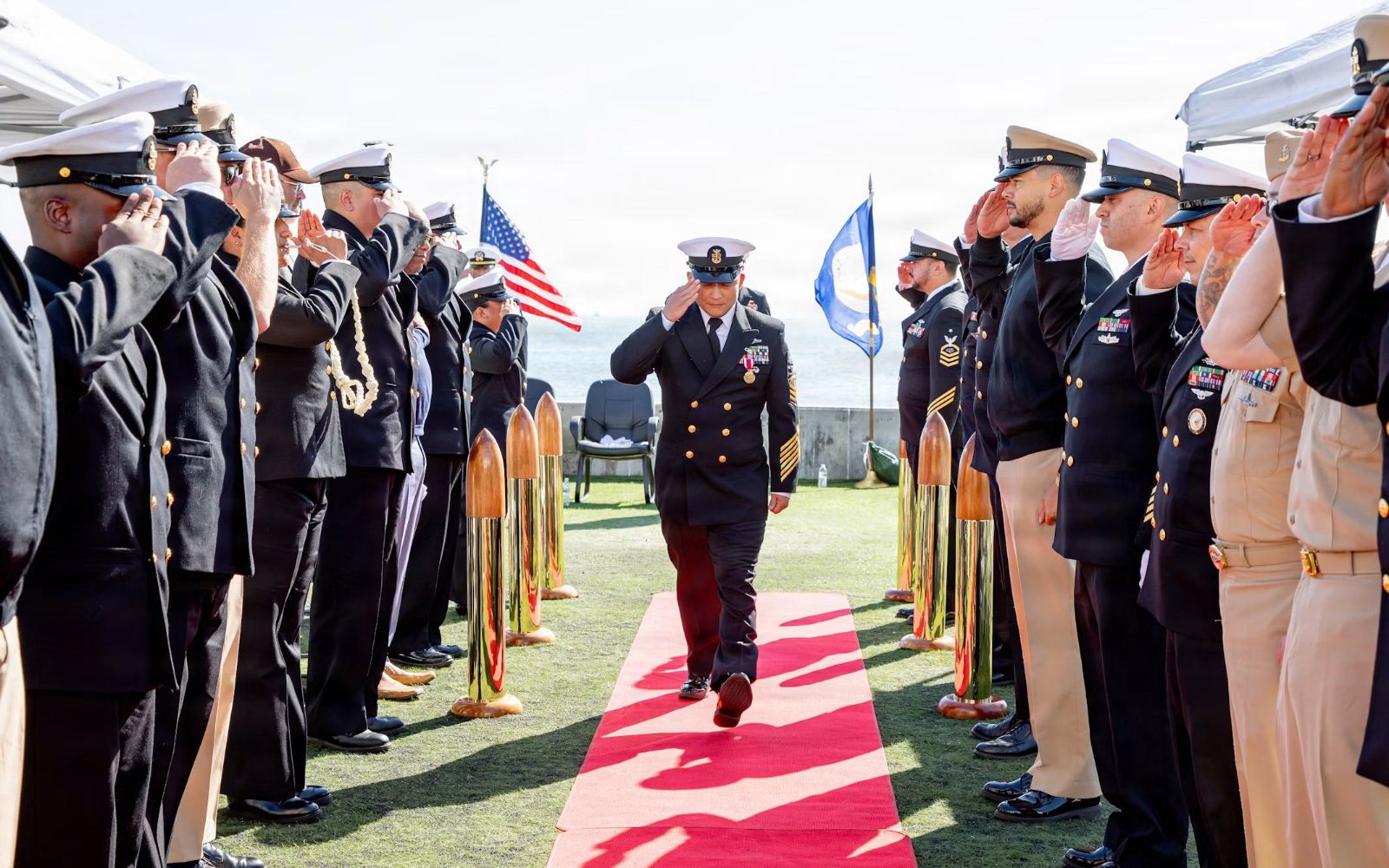 U.S. Navy officer walking through a line of saluting sailors at a ceremony